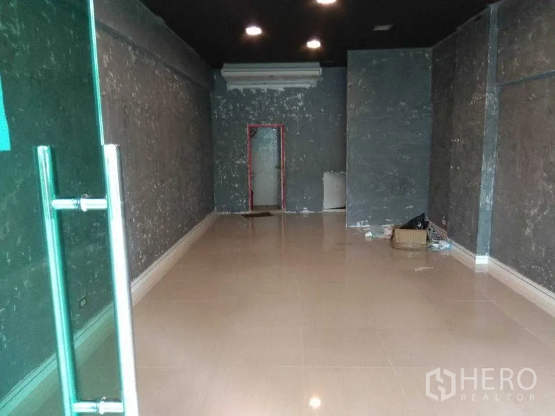 零售空间 出租在Huai Khwang, Bangkok - 空置零售单元，瓷砖地面、深色天花和筒灯，通向后方门口。