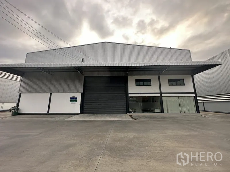 คลังสินค้า ให้เช่าในBang Phli, Samut Prakan - ด้านหน้าโกดังแสดงชายคาคลุมโหลดและประตูม้วนตรงกลาง