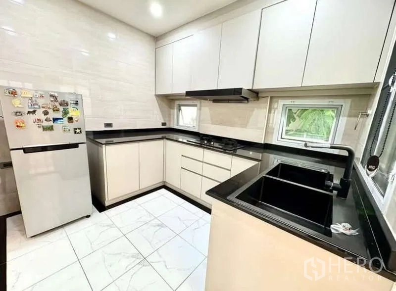 Detached House for rent in Phasi Charoen, Bangkok - Modern U-shaped kitchen with white cabinetry, black countertops and windows.