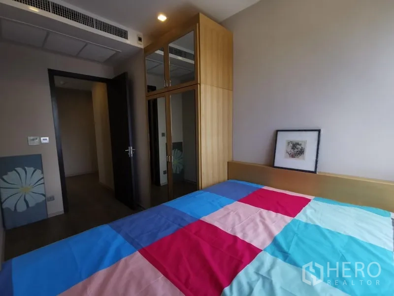 Condominium for rent or sale in Watthana, Bangkok - Cozy bedroom with colorful quilt and a built‑in mirrored wardrobe.
