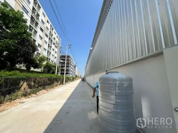 Warehouse for rent in Lat Krabang, Bangkok - Concrete access road beside a modern metal-clad warehouse with apartments and power lines under a clear sky in Lat Krabang.