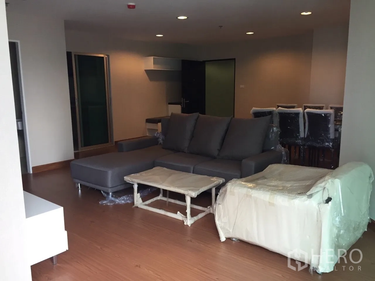 Condominium for rent in Huai Khwang, Bangkok - Spacious living room with L-shaped sofa, wood flooring and recessed lighting in a Huai Khwang condo.
