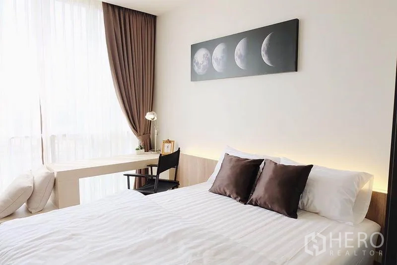 Condominium for sale in Watthana, Bangkok - Minimalist bedroom with double bed, moon phase artwork and floor‑to‑ceiling sheer curtains.