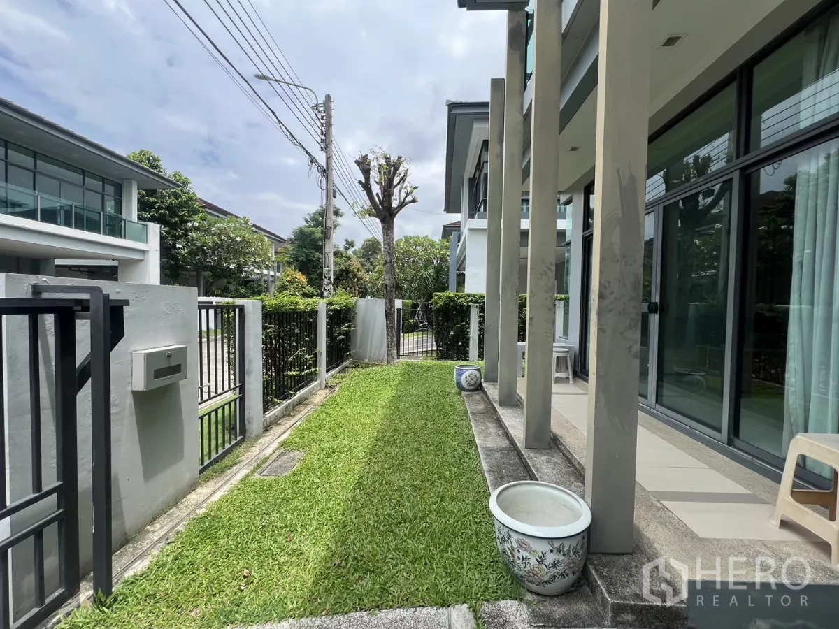 Detached House for rent in Bang Kapi, Bangkok - Front garden with green lawn, walkway, and glass sliding doors beside vertical columns.