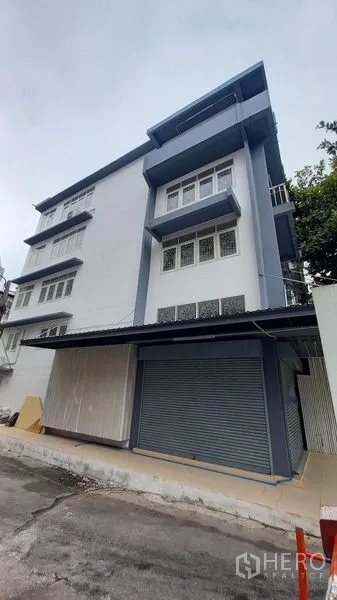 อาคารพาณิชย์ ให้เช่าในBangkok - อาคารพาณิชย์มุมตึกหลายชั้น โทนสีน้ำเงินขาว พร้อมประตูลูกกลิ้งโลหะ.