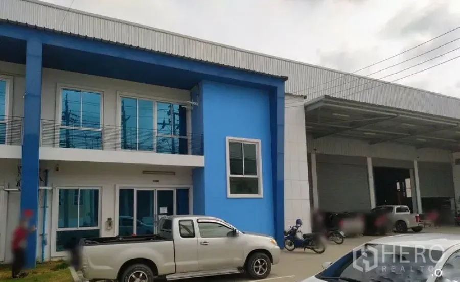 Warehouse for rent in Bang Sao Thong, Samut Prakan - Blue two-story office facade attached to a modern warehouse with covered loading bays and parking in Bang Sao Thong.