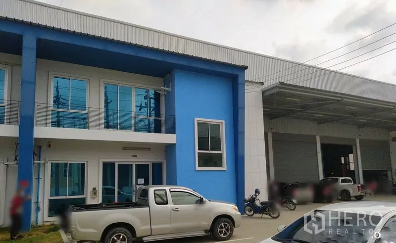 Warehouse for rent in Bang Sao Thong, Samut Prakan - Blue two-story office facade attached to a modern warehouse with covered loading bays and parking in Bang Sao Thong.