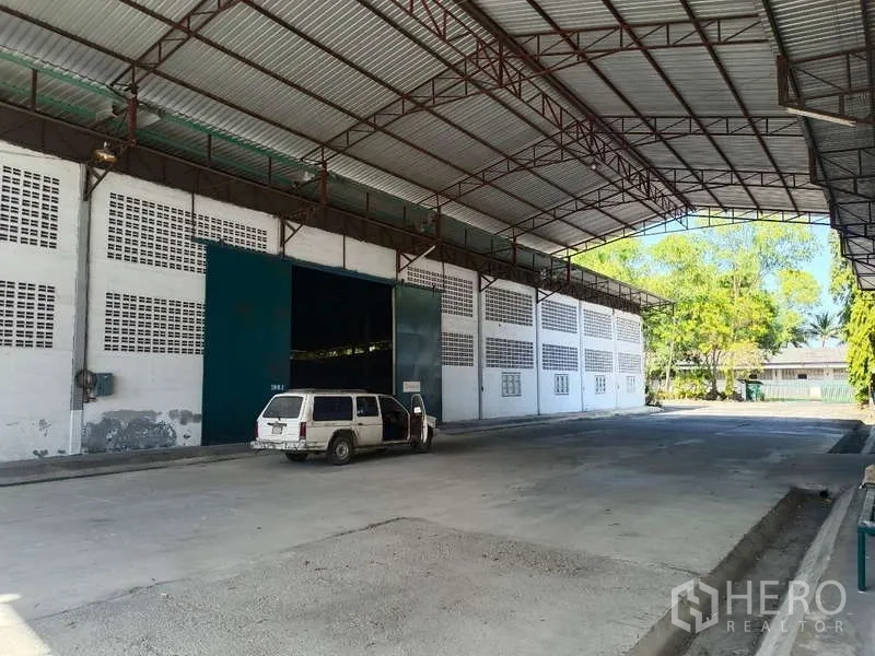 货栈 出租在Mueang Rayong, Rayong - 带高大雨棚的装卸区，仓库入口前停有车辆。