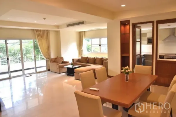 Apartment for rent in Sathon, Bangkok - Open‑plan living and dining space overlooking a greenery‑lined balcony.