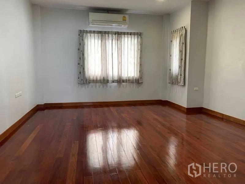 Detached House for sale in Bang Khun Thian, Bangkok - Upper-floor room with glossy hardwood floor, two curtained windows and wall AC.