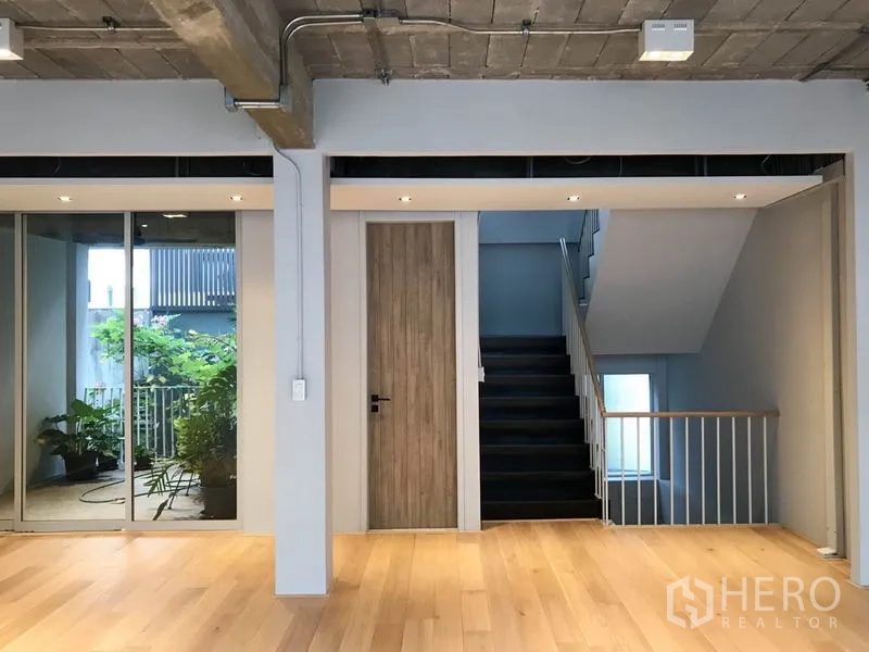 Townhouse for rent in Khlong Toei, Bangkok - Upper hallway with light wood floors, sliding glass to a balcony garden and staircase.