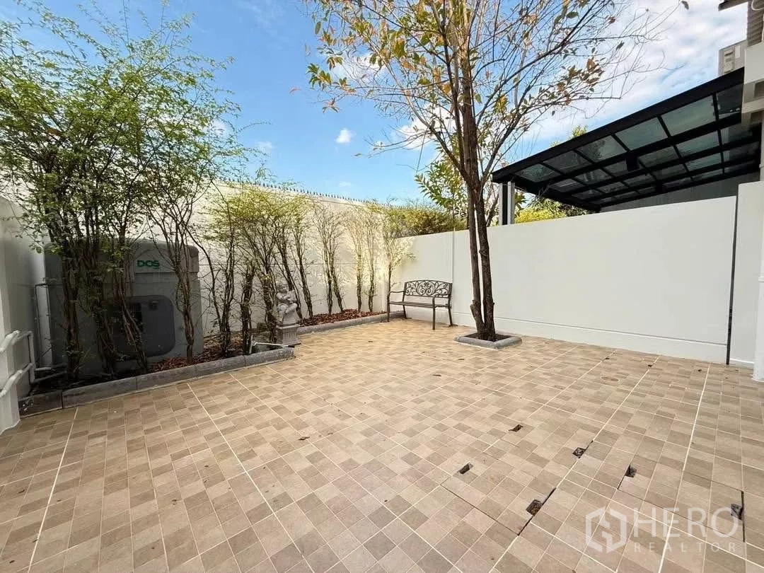 联排别墅 出租在Prawet, Bangkok - 宽阔围墙后院，有树木、长椅与开放铺装空间。