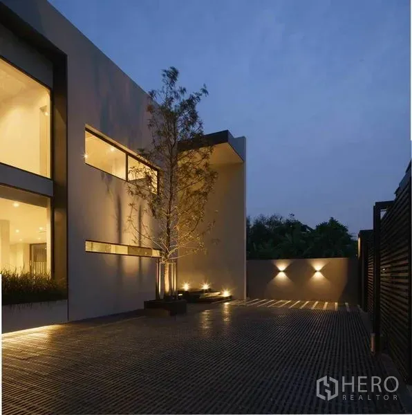 Home Office for sale in Wang Thonglang, Bangkok - Modern home office exterior in Wang Thonglang, Bangkok with lit courtyard and tree planters at dusk.
