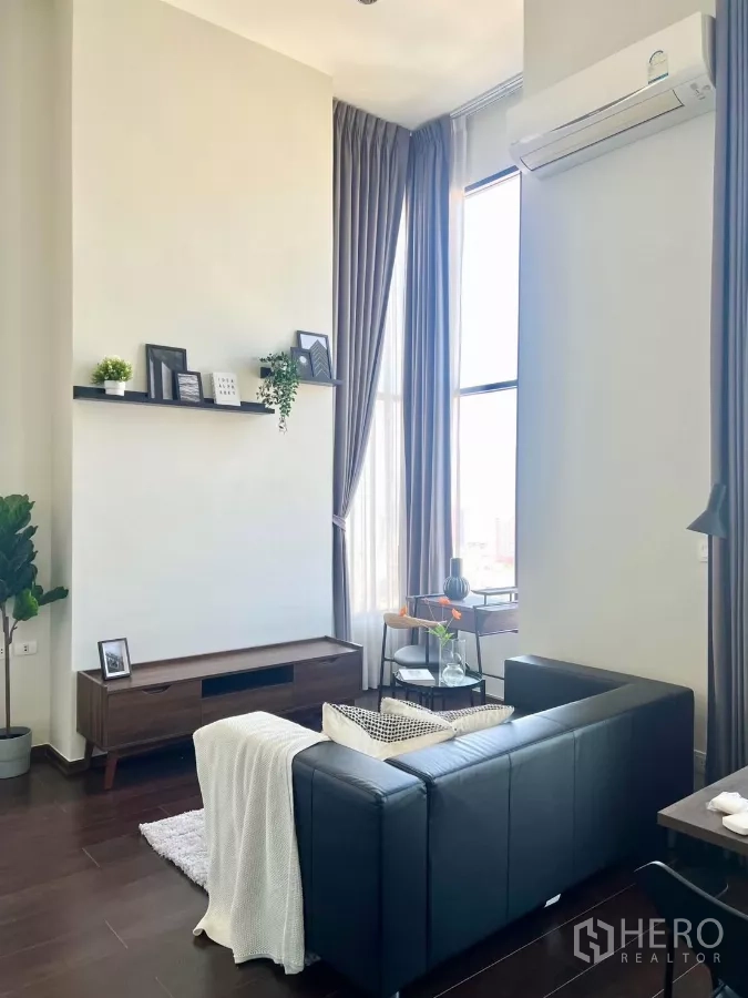 Condominium for rent in Watthana, Bangkok - Cozy seating area with black sofa, soft throw, and large corner windows.