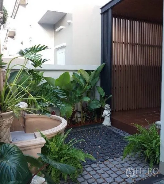 Detached House for sale in Nonthaburi - Compact landscaped garden with water feature, potted plants and stone paving beside a slatted screen.