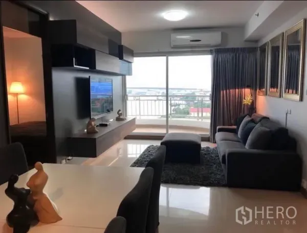 Condominium for rent in Bangkok - Open-plan living room with sofa, TV wall and dining area leading to a balcony with city and river views.
