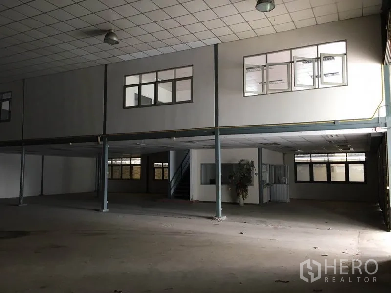 货栈 出租在Prawet, Bangkok - 仓库内部高挑空间，钢柱与吊灯，设有带窗的夹层办公室和楼梯。