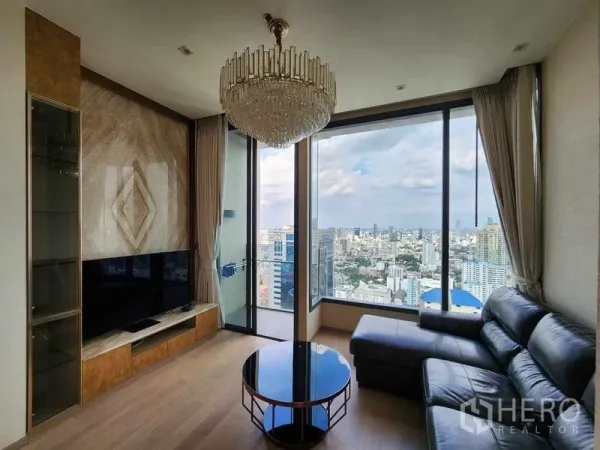 คอนโด ให้เช่า - ห้องนั่งเล่นชั้นสูง กระจกเต็มบาน โซฟาหนัง และวิวสกายไลน์กรุงเทพฯ