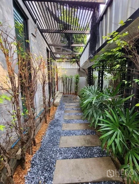 带办公室的家 出租在Lat Phrao, Bangkok - 带格栅顶的遮荫步道，碎石与混凝土踏步，两侧热带植物。