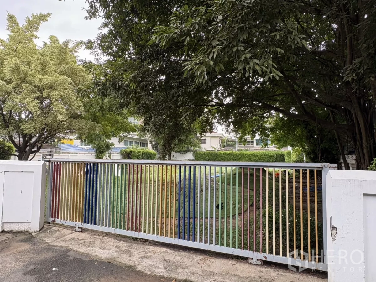 ที่ดิน ให้เช่าในWatthana, Bangkok - มุมใกล้ของประตูเหล็กหลากสี มองเห็นสนามหญ้าและต้นไม้ใหญ่ด้านใน