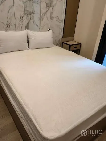 Condominium for rent in Watthana, Bangkok - Cozy bedroom with a queen bed, marble-look feature wall and bedside table.