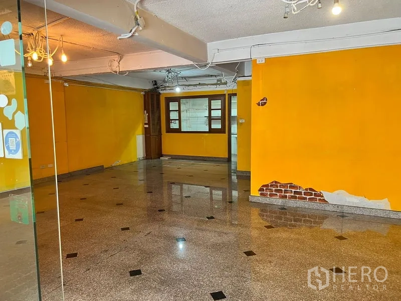 Townhouse for rent in Khlong Toei, Bangkok - Bright ground-floor space with yellow feature walls and terrazzo flooring.