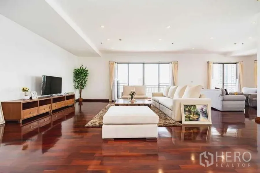 房间 出租在Sathon, Bangkok - 宽阔客厅，白色沙发、电视柜、亮面木地板与多扇落地窗。