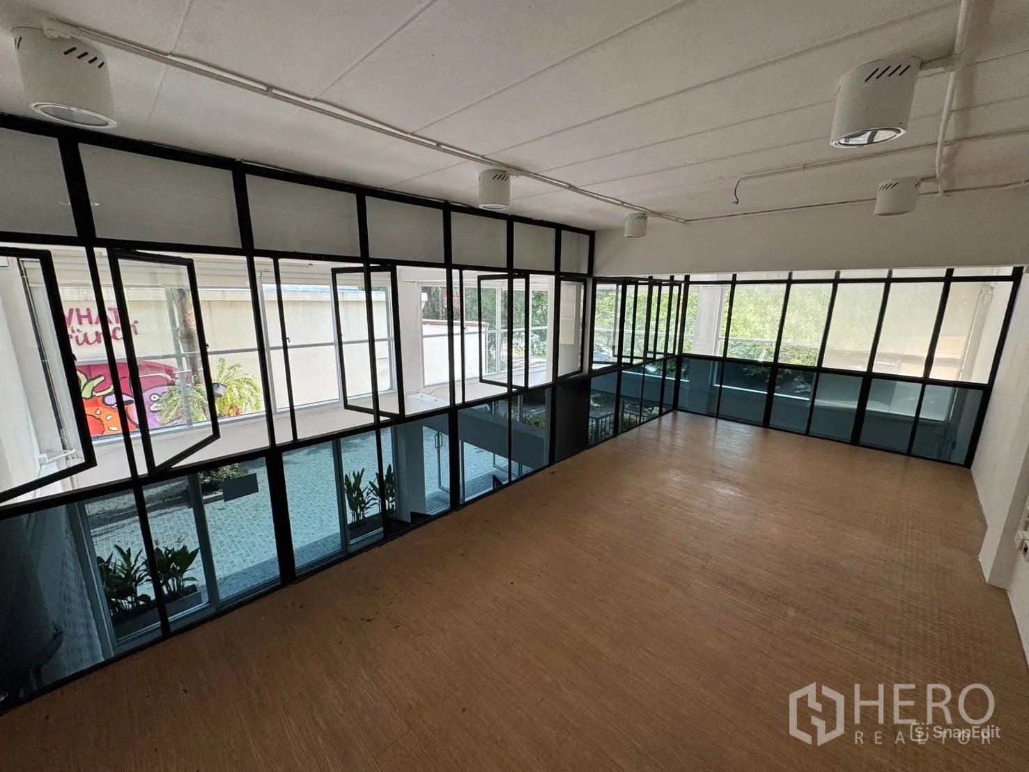 店屋 出租在Wang Thonglang, Bangkok - 宽敞夹层，黑框落地窗俯瞰庭院与绿植。
