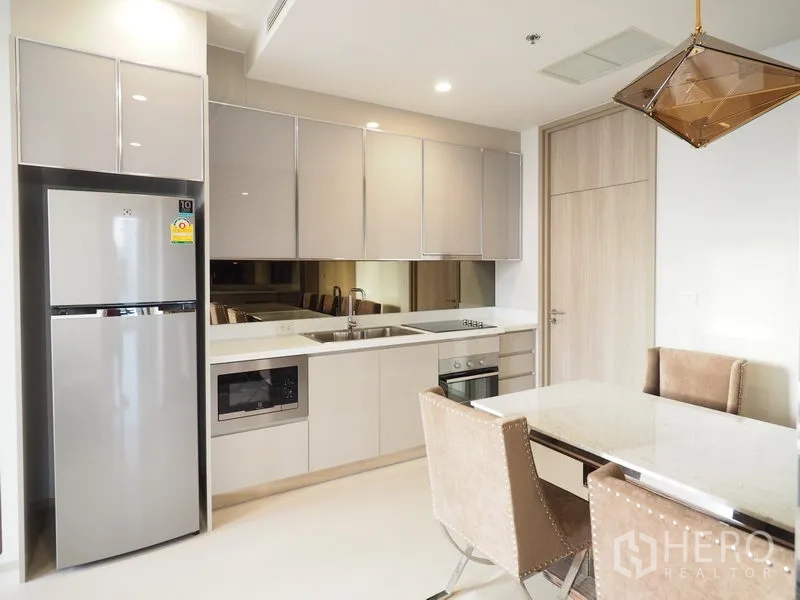 Condominium for rent in Pathum Wan, Bangkok - Sleek kitchen with full-size fridge, cooktop, microwave and dining table with upholstered chairs.
