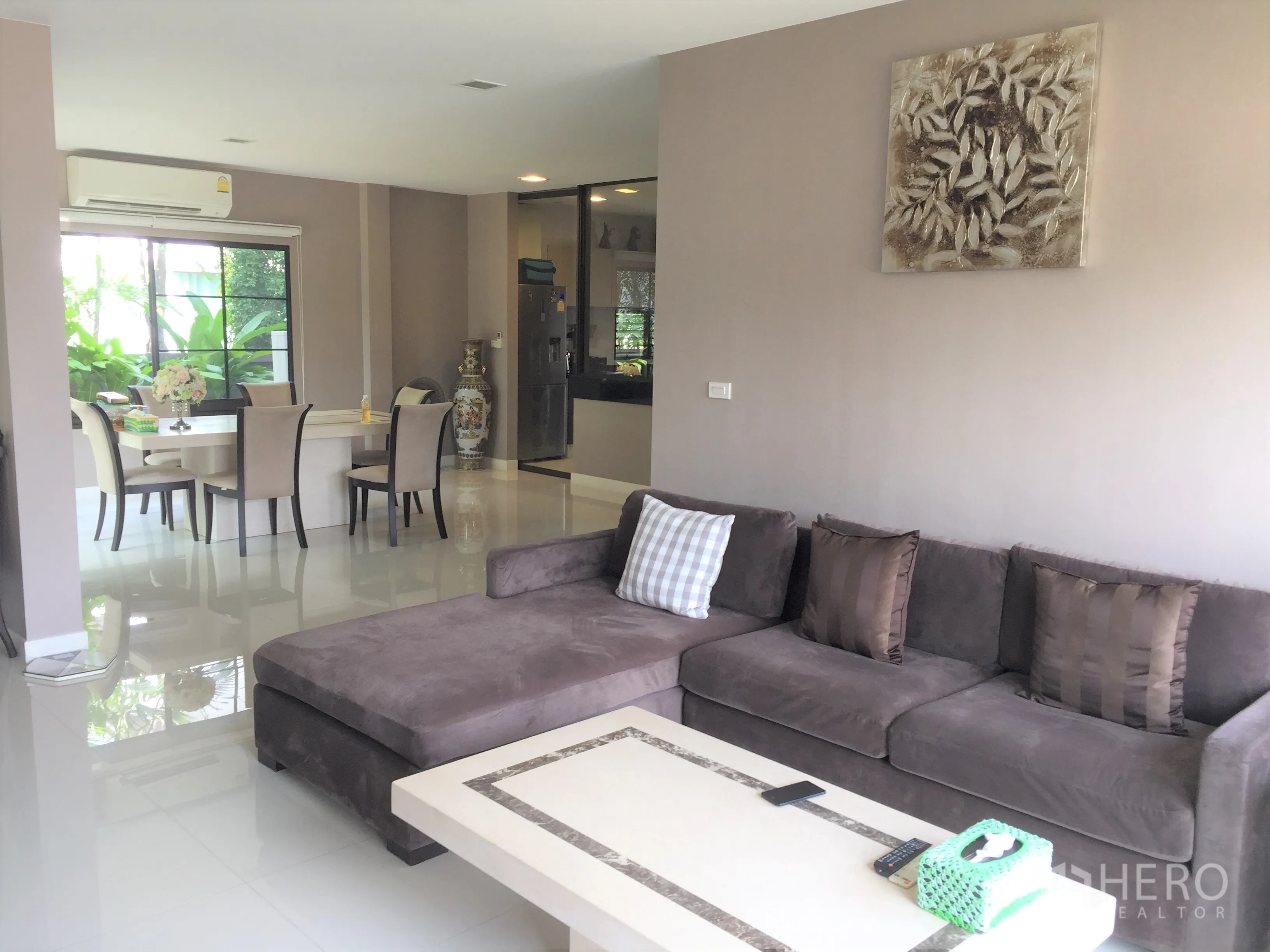 Detached House for rent or sale in Prawet, Bangkok - Bright open-plan living and dining area with L-shaped sofa, glossy tile floors and large garden-facing windows.