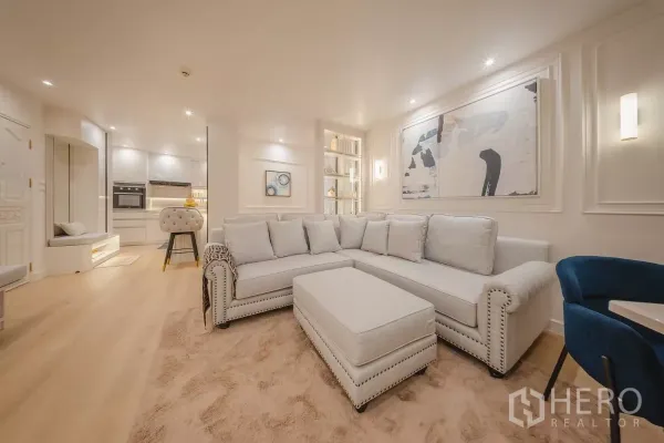 Condominium for rent in Yan Nawa, Bangkok - Bright open-plan living room with L-shaped sofa, abstract artwork and recessed lighting beside a modern kitchen.