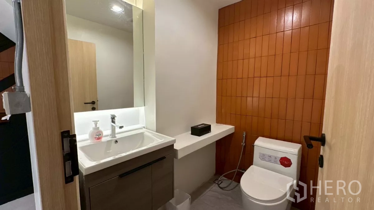 Home Office for rent in Watthana, Bangkok - Guest bathroom with vanity and toilet featuring an orange tile accent wall.