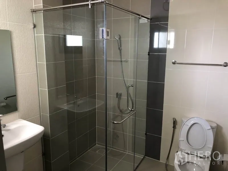 独立式住宅 出租在Prawet, Bangkok - 卫浴带转角玻璃淋浴间、座便器与小型台盆。