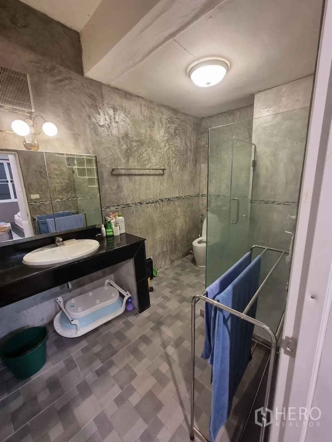 Townhouse for rent in Din Daeng, Bangkok - Modern bathroom with concrete-finish walls, glass shower and long counter.