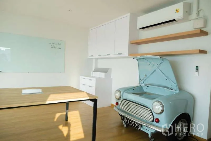 Home Office for rent in Phra Khanong, Bangkok - Creative office room with wooden desk, wall shelves and a classic Mini car front used as decor.