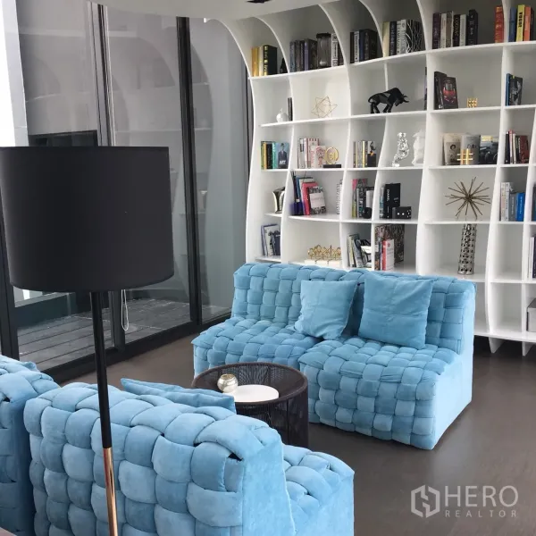 公寓 出租在Watthana, Bangkok - 住户图书休闲区，蓝色沙发与弧形白色书架，采光充足。