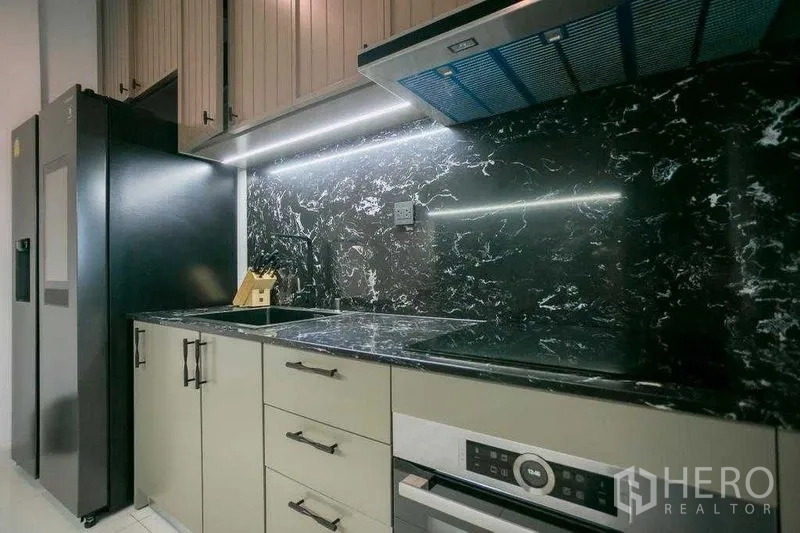 Detached House for rent in Bangkok - Modern pantry kitchen with black marble backsplash, built-in hob, oven and tall refrigerator.