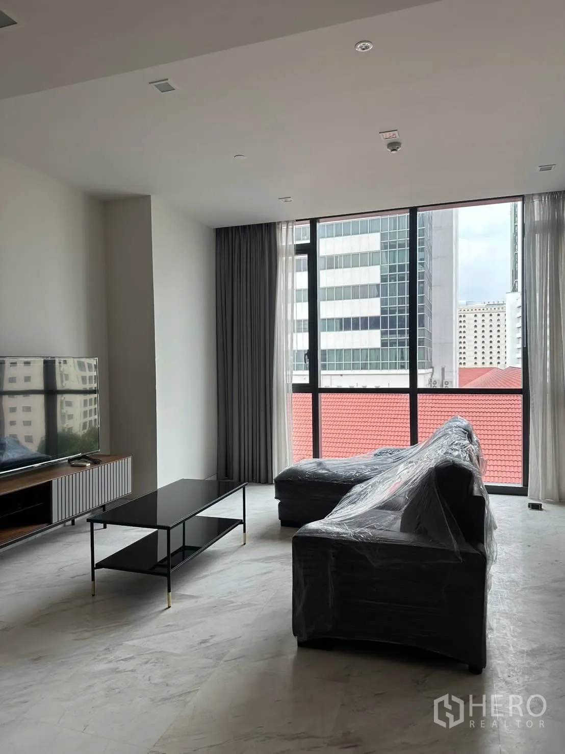Condominium for rent or sale in Watthana, Bangkok - Bright living room with L-shaped sofa, TV console, and floor-to-ceiling windows.