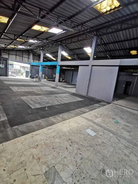 货栈 出租在Nonthaburi - 开放式仓库内部，钢桁架屋顶、采光窗与灰色隔间。