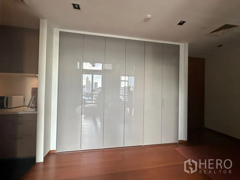 Condominium for rent or sale in Sathon, Bangkok - Hallway with glossy built-in wardrobes and a glimpse of the living area and kitchenette.