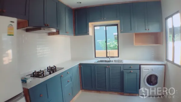 Detached House for rent in Suan Luang, Bangkok - Modern kitchen with blue cabinetry, white subway tile backsplash, gas hob, double sink, and windows.
