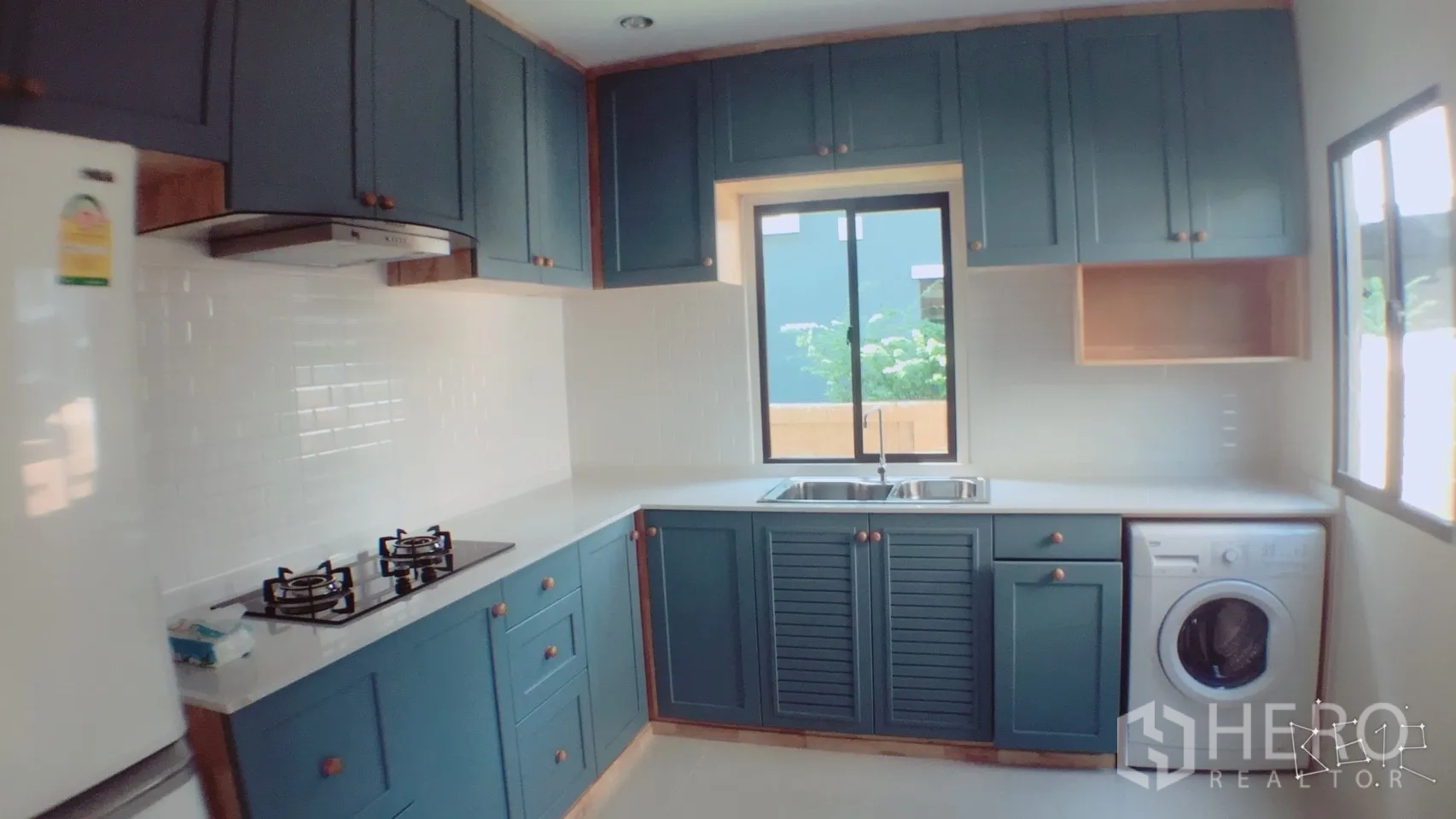 Detached House for rent in Suan Luang, Bangkok - Modern kitchen with blue cabinetry, white subway tile backsplash, gas hob, double sink, and windows.