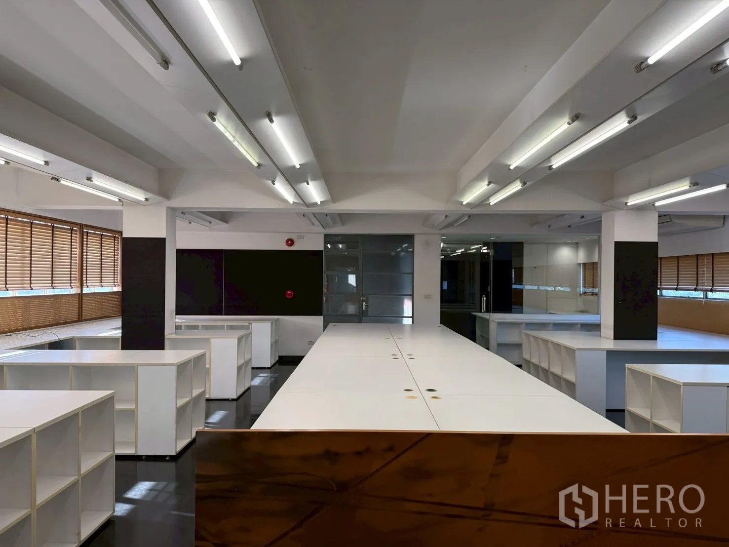 Office Space for rent in Huai Khwang, Bangkok - Open-plan office with long white workstations, fluorescent lights, glass partition and built-in shelving.