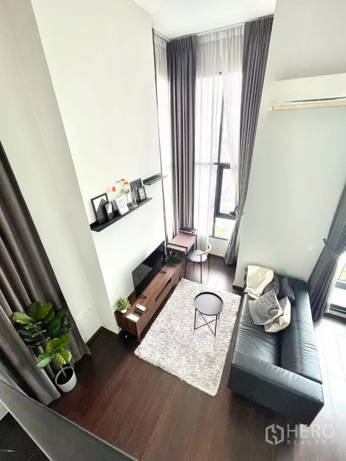 Condominium for rent in Watthana, Bangkok - Loft-style living room with double-height ceiling, dark wood floors, and floor-to-ceiling windows.