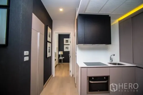 Condominium for rent in Khlong San, Bangkok - Compact modern kitchen with built-in oven, induction cooktop and ample cabinetry along a hallway.