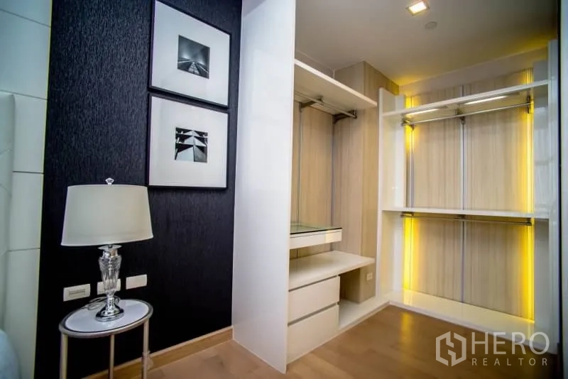 Condominium for rent in Khlong San, Bangkok - Walk-in closet with illuminated shelving, hanging rails and drawers beside the bedroom.