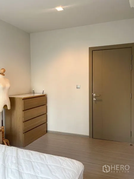 Condominium for sale in Ratchathewi, Bangkok - Bedroom corner showing wooden dresser, neutral walls, and a closed interior door.