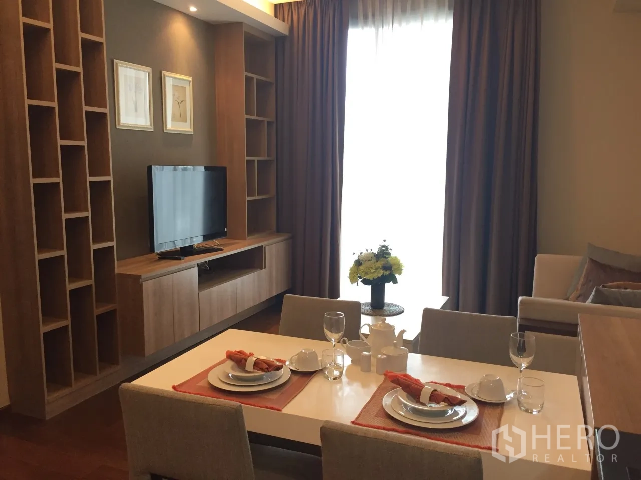 Condominium for rent or sale in Watthana, Bangkok - Dining table set facing TV wall and tall curtains brightening the living room.