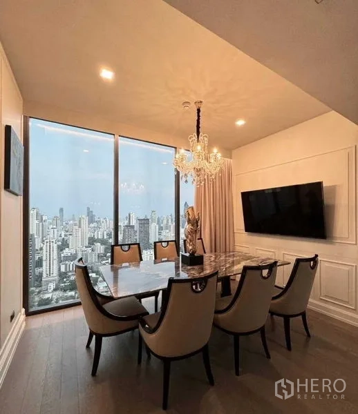 Condominium for rent in Watthana, Bangkok - Elegant dining room with a marble table, crystal chandelier, wall-mounted TV, and skyline backdrop.