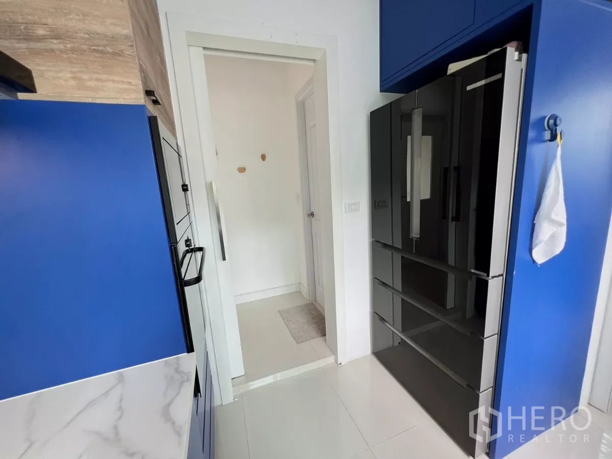 独立式住宅 出租或出售在Khlong Luang, Pathum Thani - 厨房入口，大型黑色冰箱与蓝色柜体